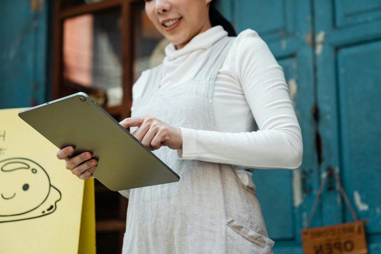 Smiling woman with a tablet in front of a shop displaying an open sign.